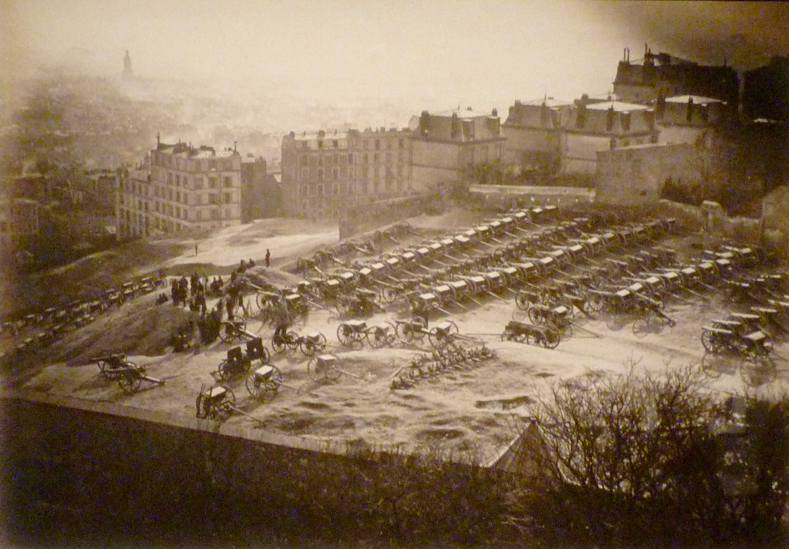 Rows of field guns parked on the bare summit of Montmartre in 1871, with Paris in the haze below