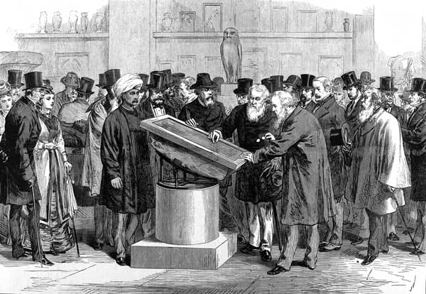 Scholars in top hats crowd round the Rosetta Stone, tilted on a round stand in a gallery of the British Museum